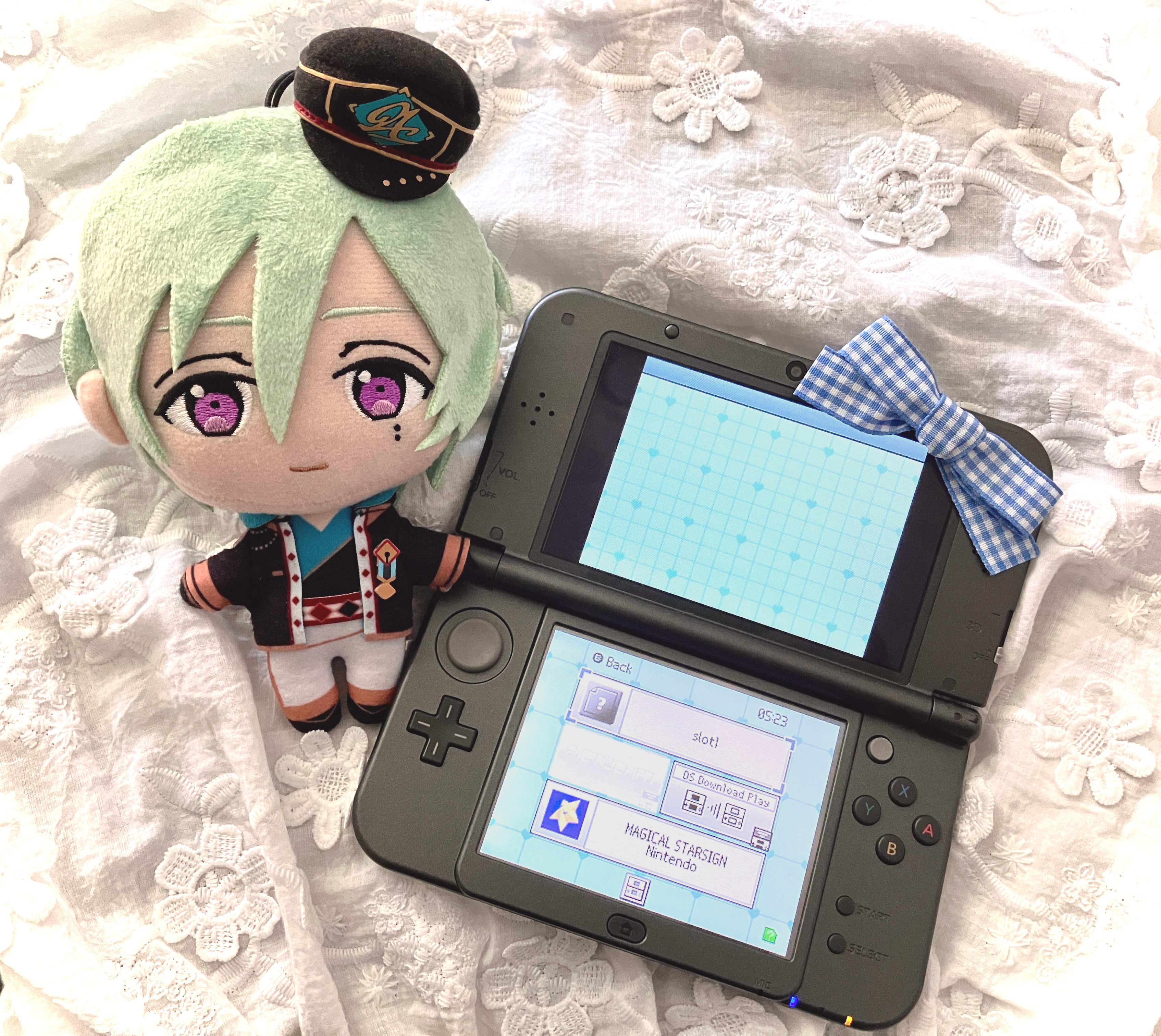 Tatsumi KAzehaya plush lying left to a 3ds displaying a custom blue dsi theme, to the right is a blue gingham ribbon. Underneath is a white cloth embroidered with flowers